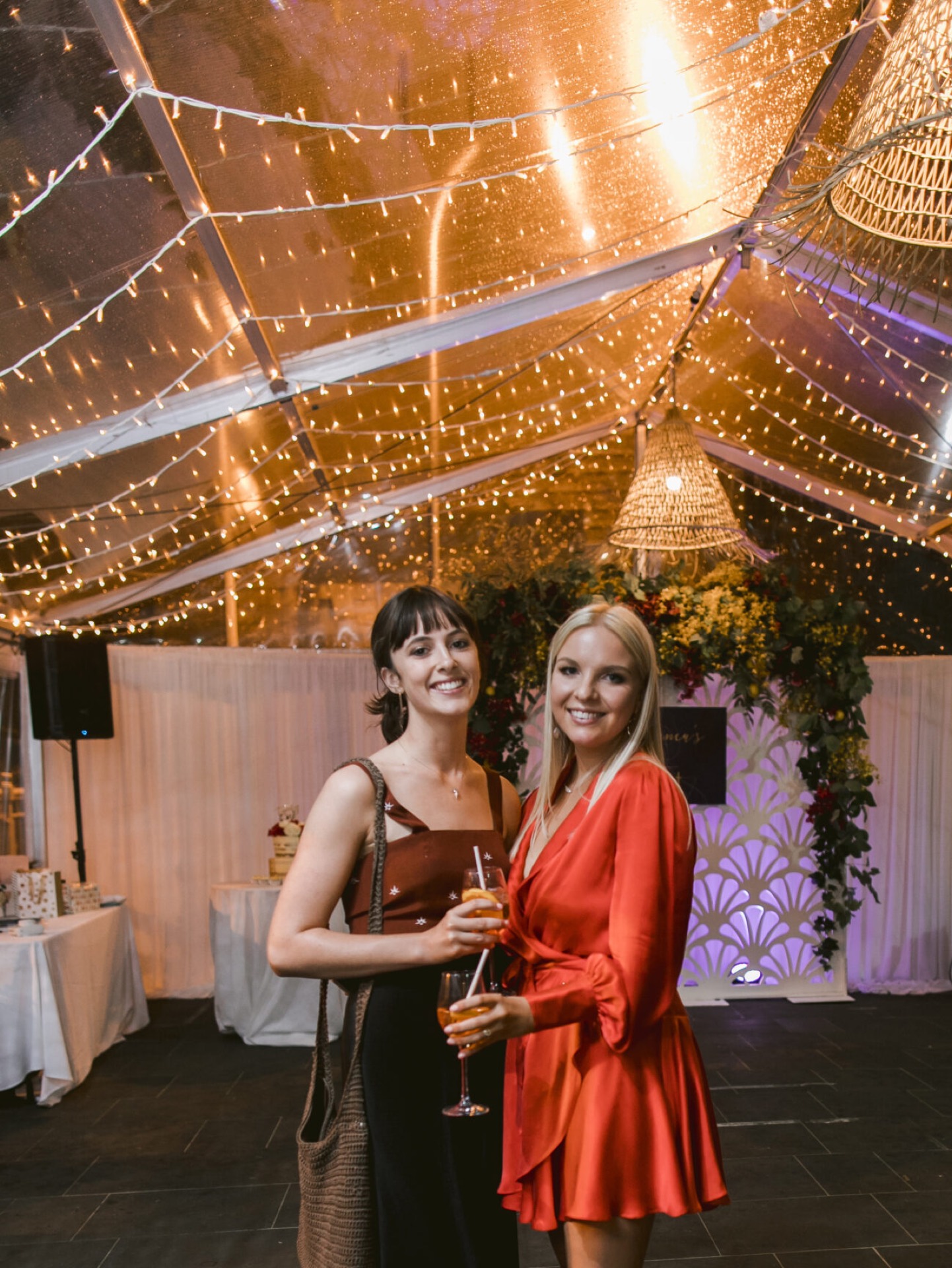 Two guests with cocktails at a birthday party under fairy lights in the marquee at Pier One