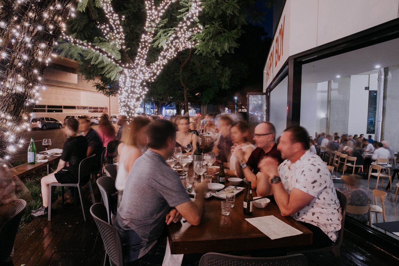 Happy Boy's outdoor deck at night, tables full of guests dining under trees wrapped in fairy lights