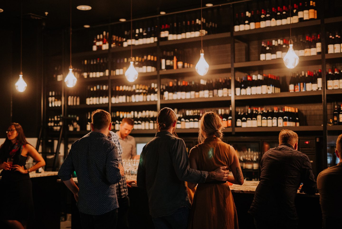 Guests standing at the marble bar beneath Snack Man's ceiling-high wine wall holding more than 500 bottles