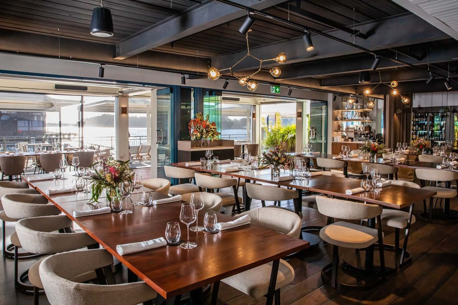 The main dining room at PIER dining set with long timber tables, opening onto the terrace and Sydney Harbour